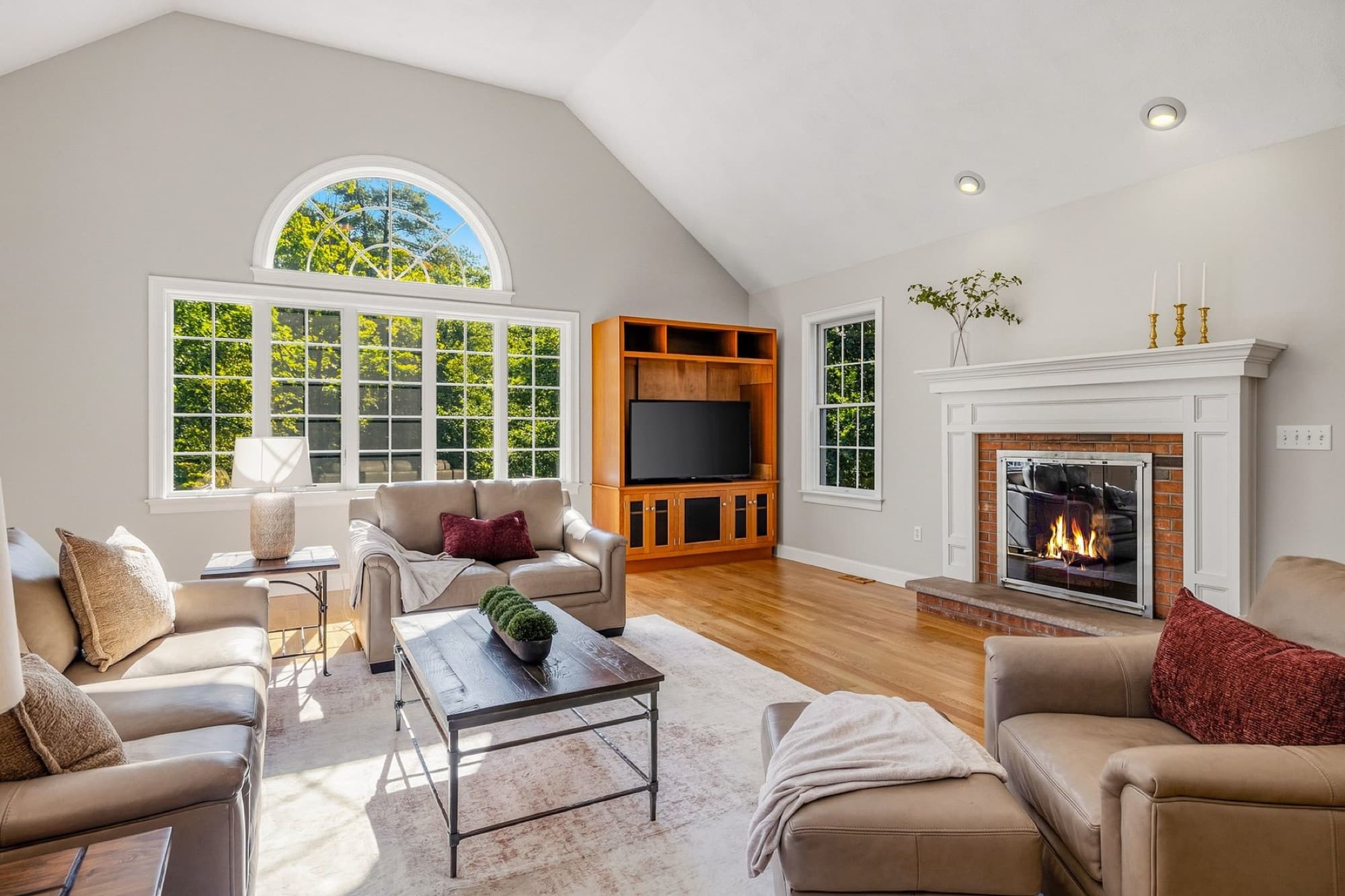The living room with the brick fireplace, a cathedral ceiling, an arched window, and built-in cabinets