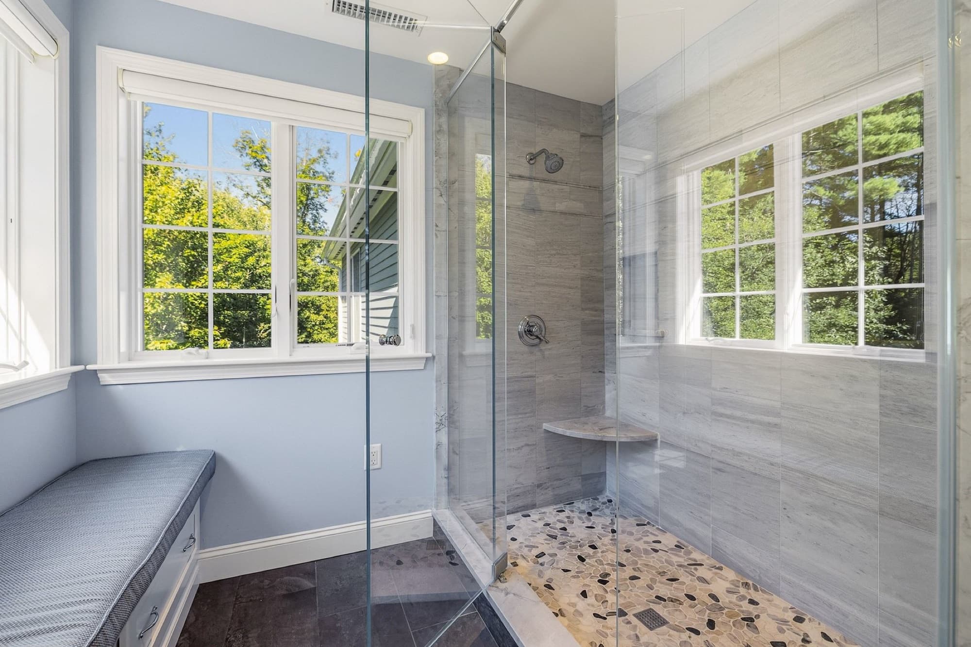 The primary bath's glass-walled tiled shower with a pebble floor and 2 windows