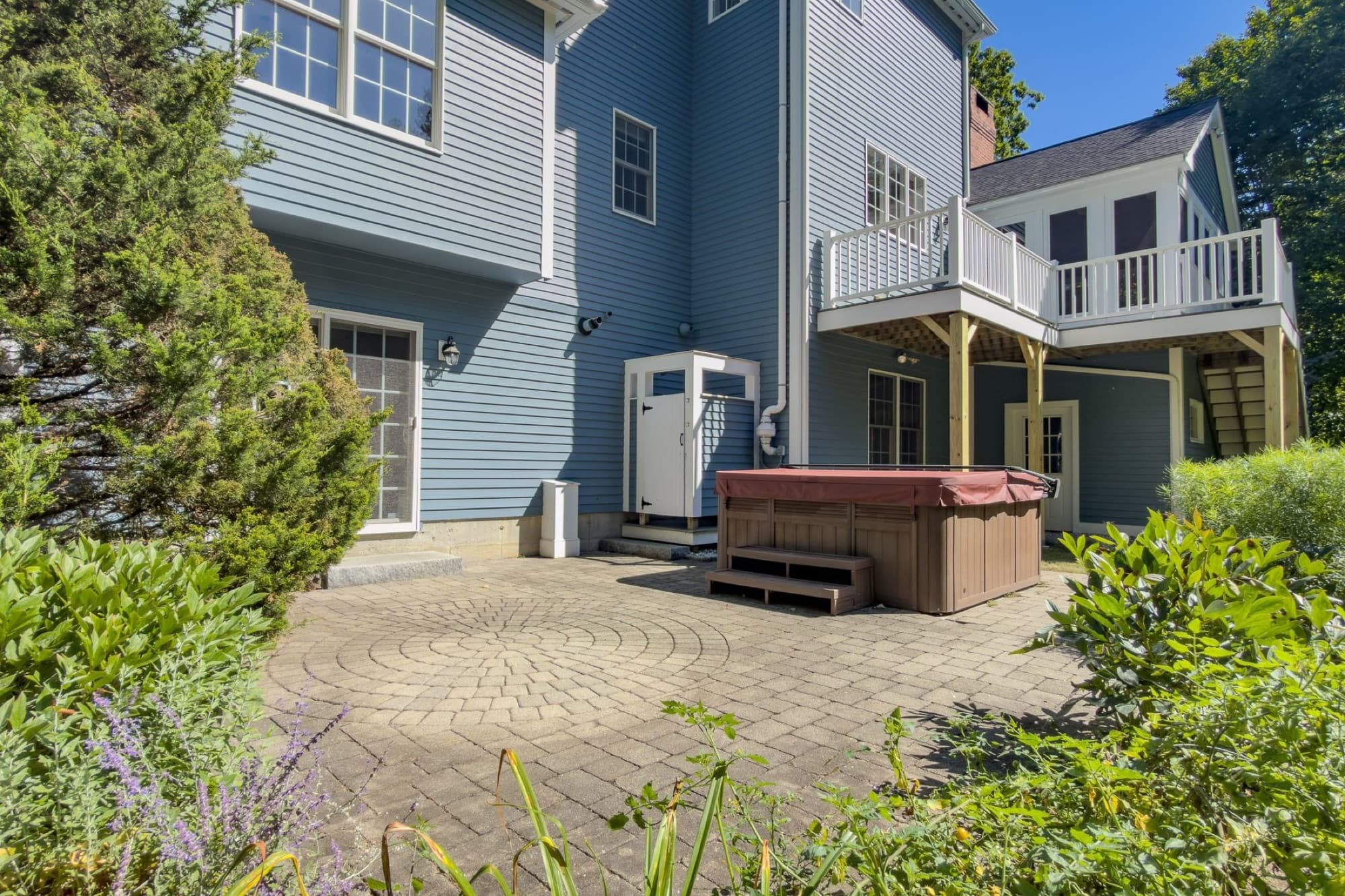 The paver patio with the hot tub and the outdoor shower on the back wall